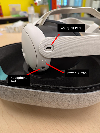 Left side of a white Meta Quest 3, each component is labeled. The charging port is an oval shape, located in the middle of the left-side strap. The power button is round, located on the left side of the headset. The headphone port is round, located on the left side of the headset, directly under the power button.