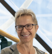 head shot photo Eva Revitt, smiling, hair pulled back and wearing glasses